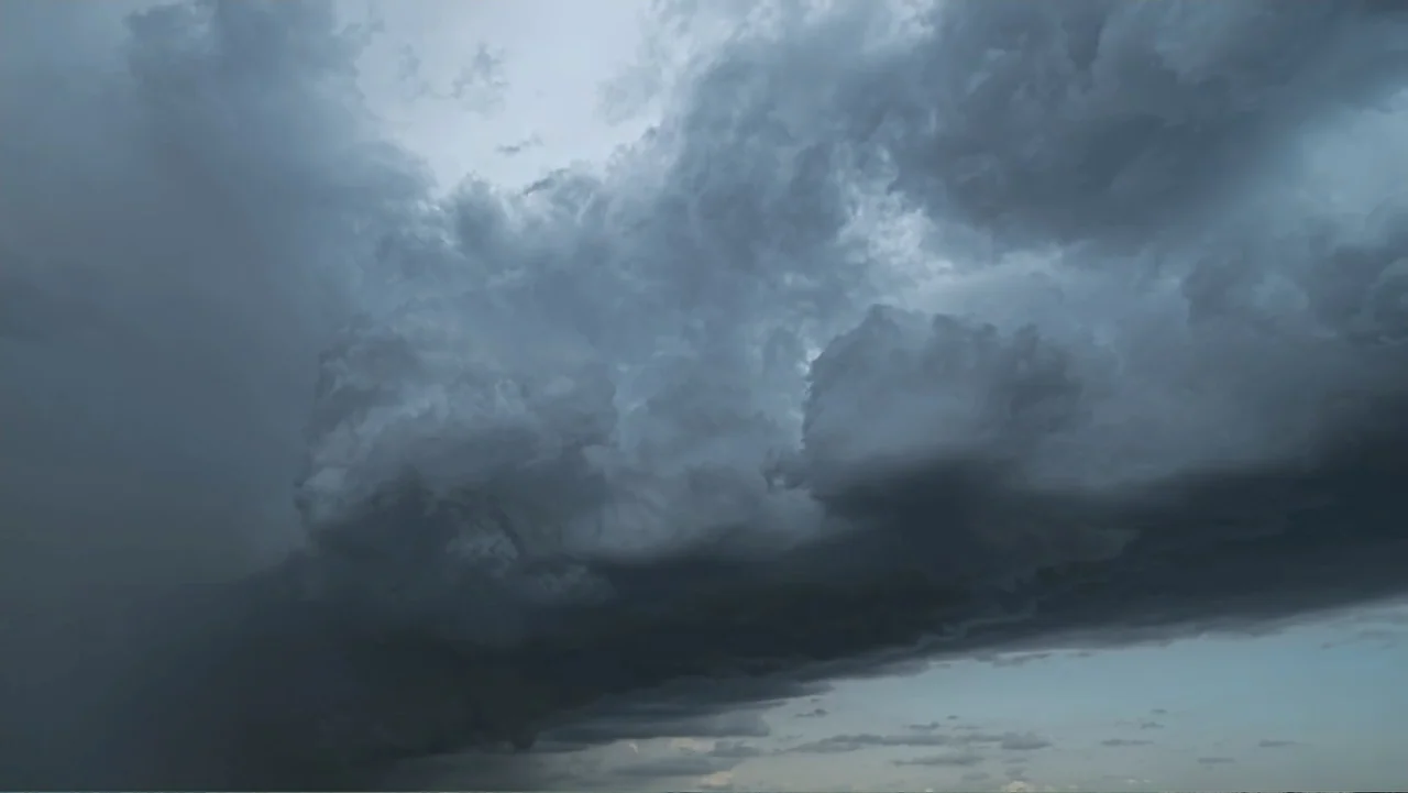 Common Ground (2000) movie still: establishing — A dense formation of dark storm clouds fills the frame against a lighter horizon. The cumulonimbus…