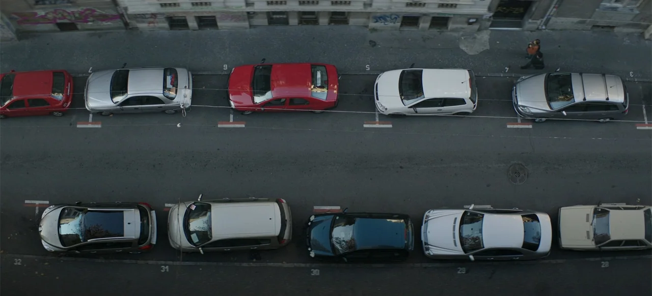 Morir un Poco (1967) movie still: establishing — An aerial top-down view of a city street showing two parallel rows of parked cars. Painted parking…
