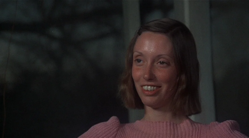 Thieves Like Us (1974) movie still: closeup — A dimly lit room with a dark, blurred background visible through a large window. A woman wearing a…