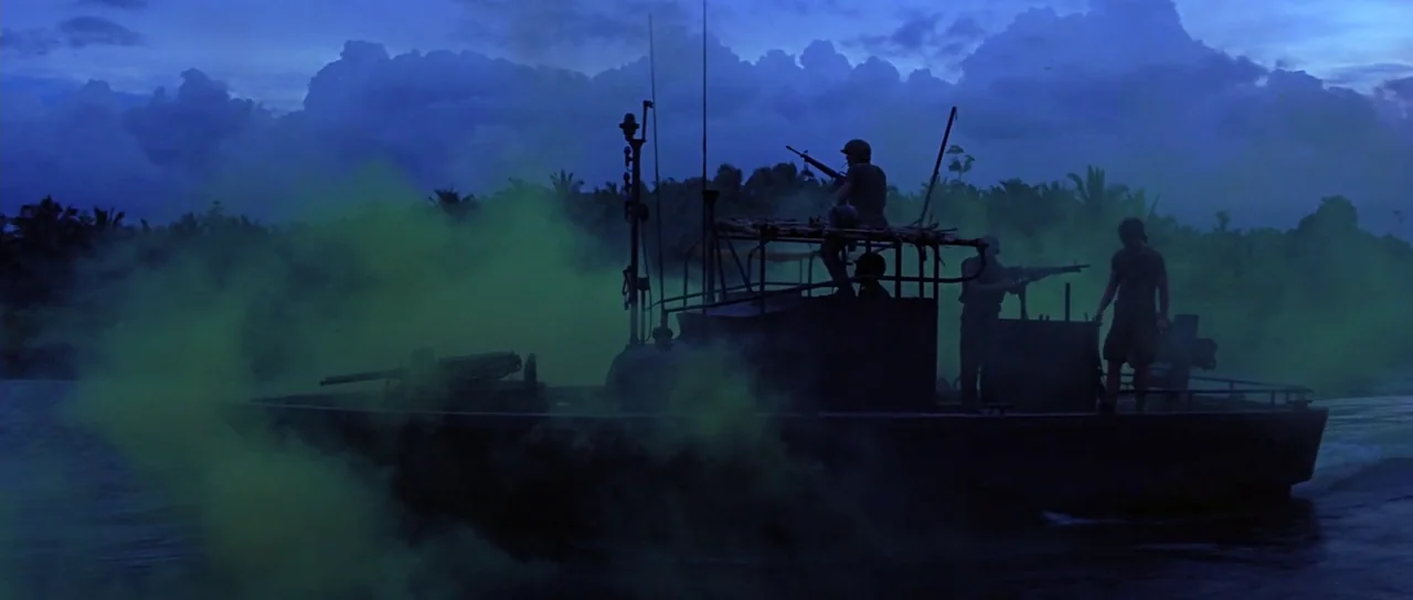 Apocalypse Now (1979) movie still: wide — A military patrol boat navigates a dark river surrounded by a dense jungle treeline. Thick green smoke…
