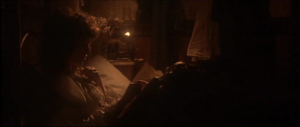 McCabe & Mrs.Miller (1971) movie still: medium — A dark, dimly lit room contains a person reading in a bed. A small lit candle rests on a nightstand…
