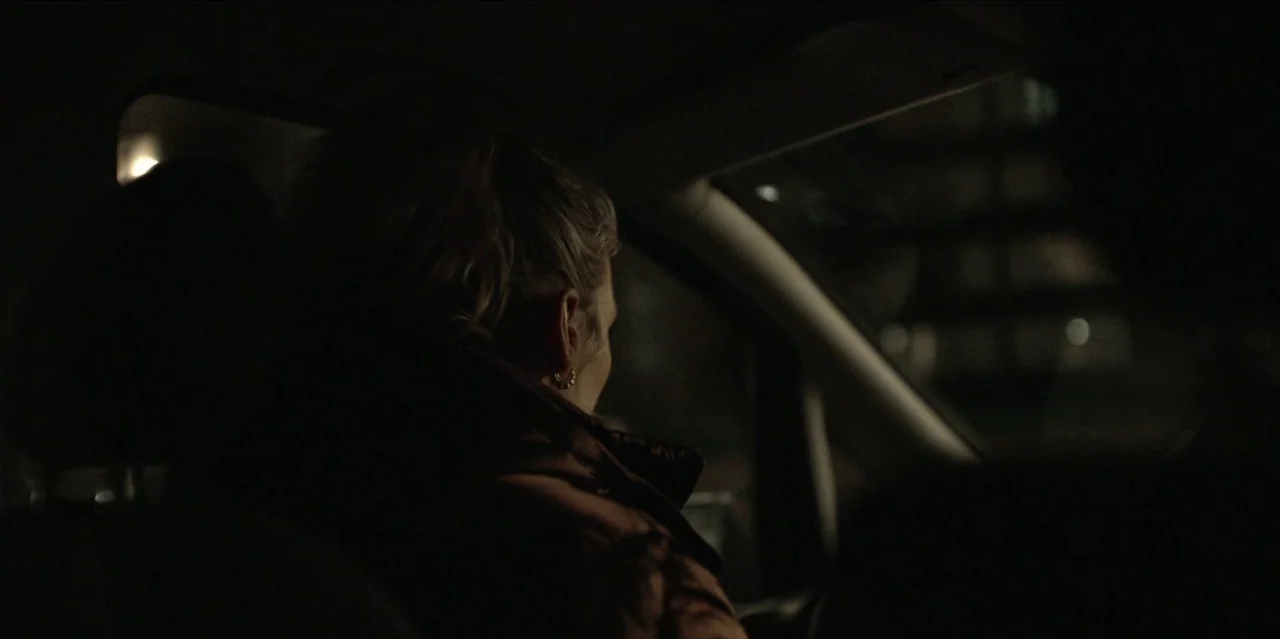 Help (2021) movie still: medium — A dark car interior at night with a person sitting in the passenger seat. The subject gazes out the side window…