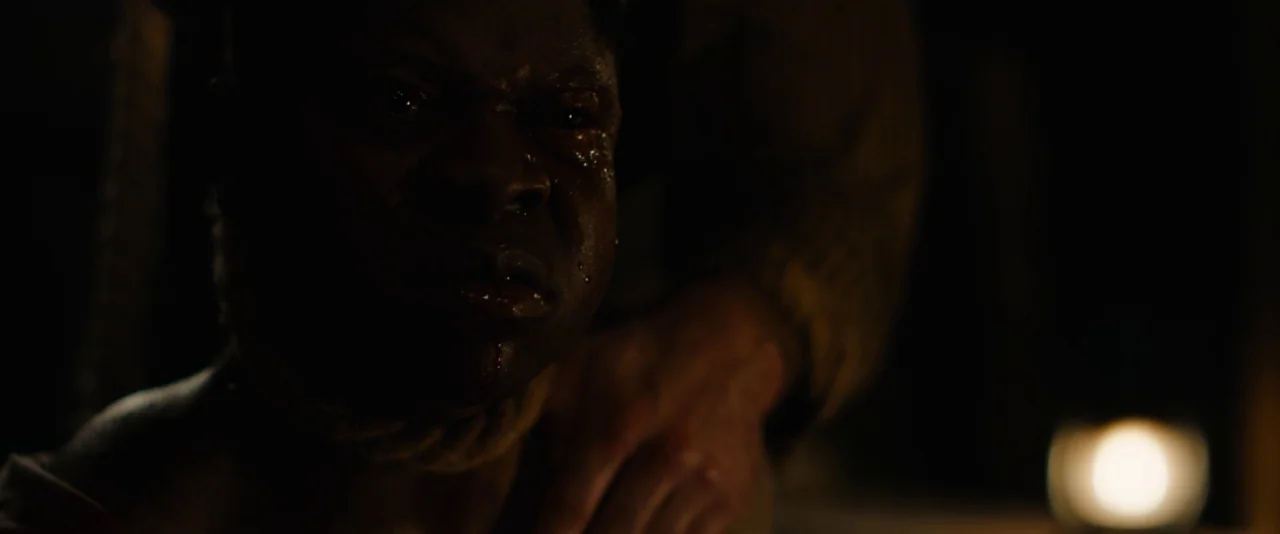 Mudbound (2017) movie still: closeup — A dimly lit room provides the backdrop for a close-up of a man. A thick rope rests tightly around the man's…