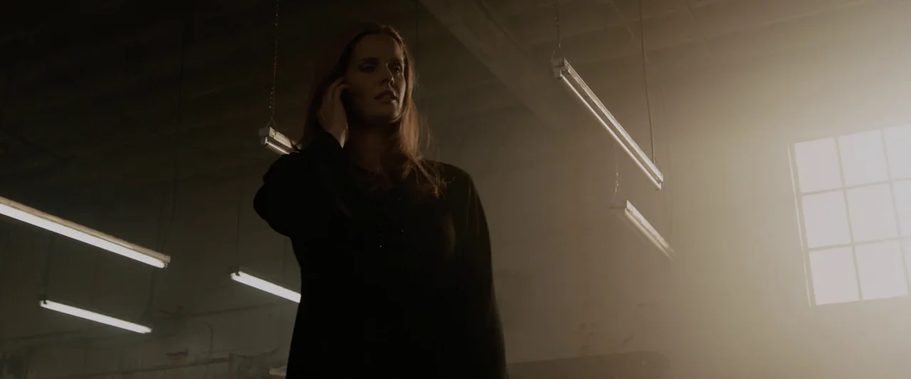 Iron Man 3 (2013) movie still: medium — A dimly lit industrial space contains hanging fluorescent lights and heavy atmospheric dust. A woman in a…