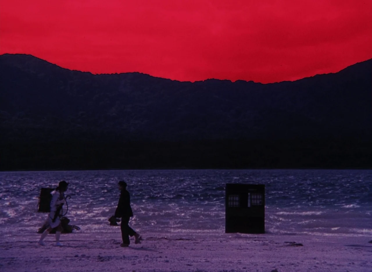 Pastoral To Die In The Country (1974) movie still: wide — A dark beach meets a deep purple sea under an intense, saturated red sky. Two figures walk…