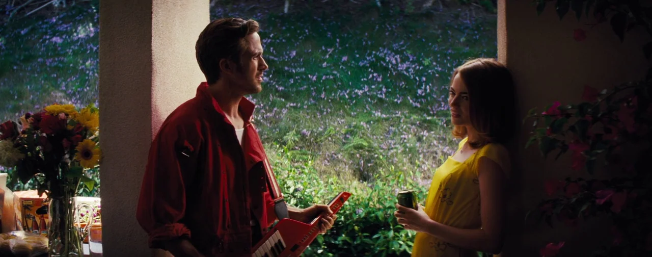 La La Land (2016) movie still: medium — A shaded patio area overlooks a sunlit field covered in purple flowering plants. A man with a red keytar and…