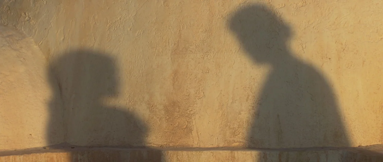 Star Wars: Episode II – Attack of the Clones (2002) movie still: closeup — A textured beige desert wall catches the shadows of two figures. The…