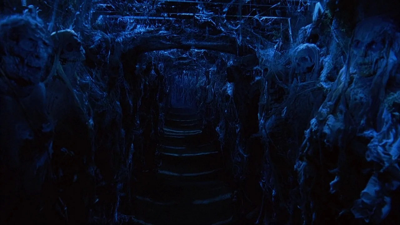 House of 1000 Corpses (2003) movie still: wide — A dark subterranean tunnel contains rows of skeletal remains draped in tattered fabric. The narrow…