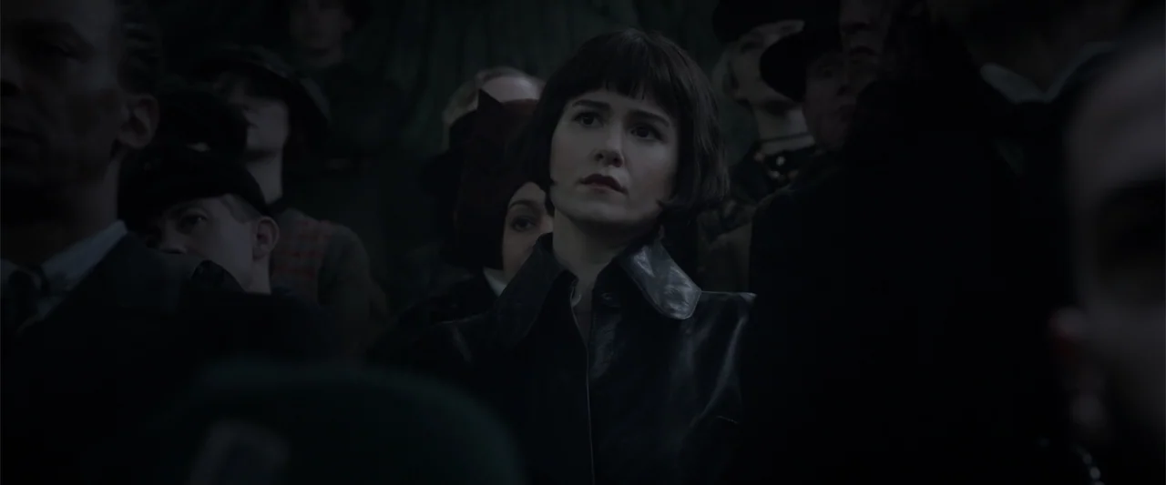 Fantastic Beasts: The Crimes of Grindelwald (2018) movie still: medium — A dark, crowded assembly hall with numerous people seated in shadows. A…