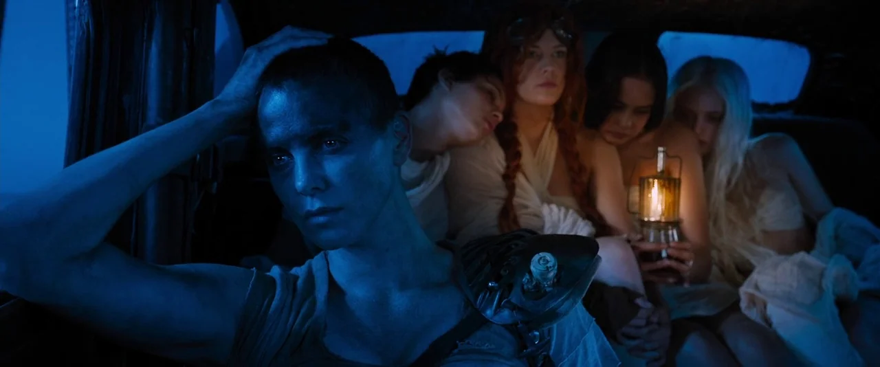 Mad Max: Fury Road (2015) movie still: medium — Inside a moving vehicle at night, four women sit together in the dim light. One woman holds a small…