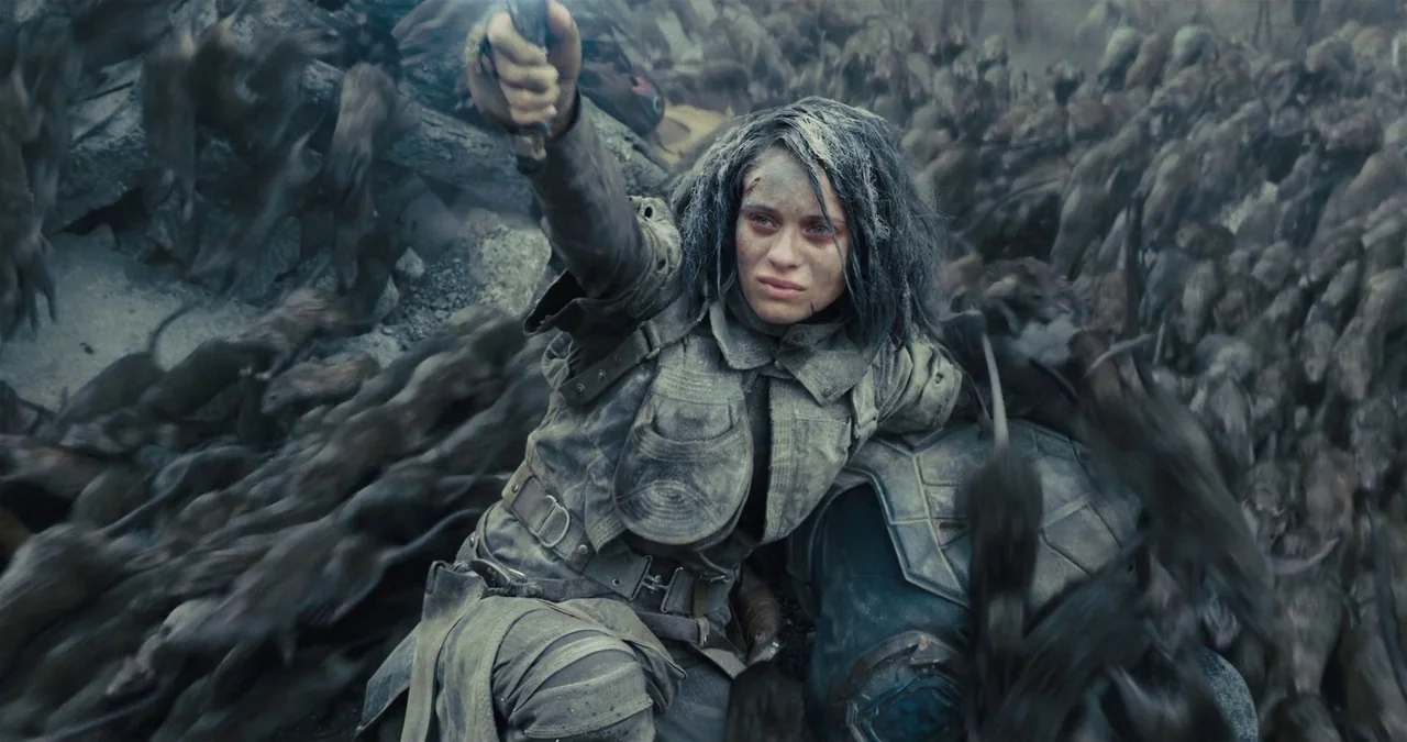The Suicide Squad (2021) movie still: medium — A woman crouches amidst a massive swarm of rats on a rugged, stone-strewn surface. She holds a…