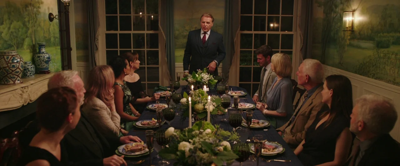Swallow (2020) movie still: wide — An elegant dining room features mural-painted walls and a long blue-clothed dinner table. A man in a suit stands…