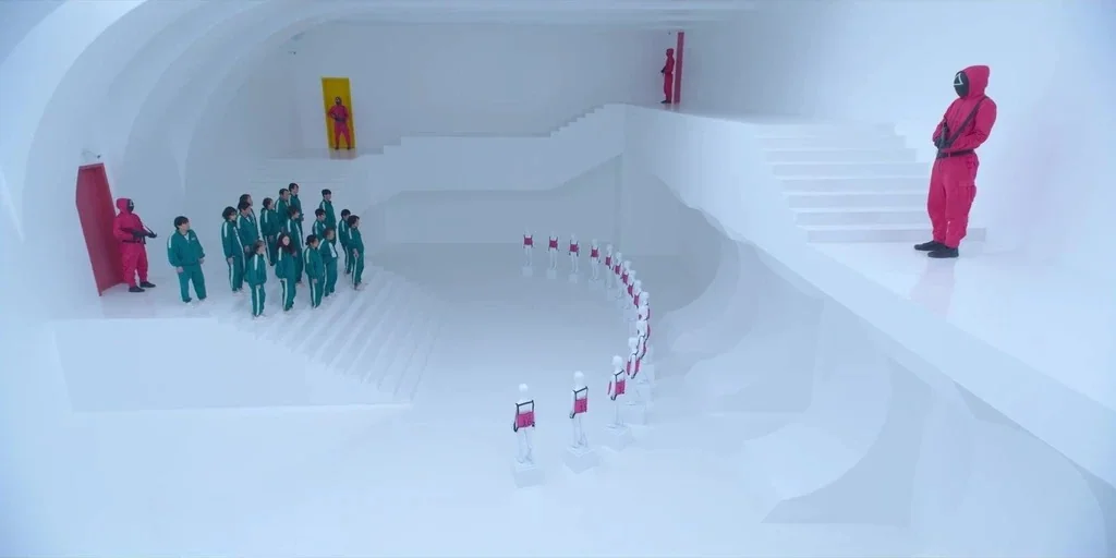 Making of: Squid Game (2021) movie still: wide — A sterile, all-white environment features curvilinear walls, platforms, and staircases. Masked…