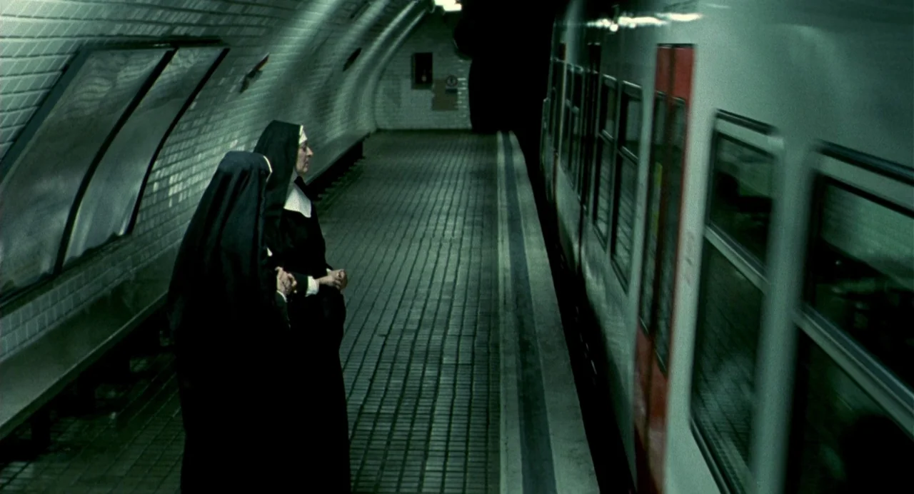 The Nameless (1999) movie still: fullbody — Two nuns in traditional black habits stand on a tiled subterranean train station platform. A white…