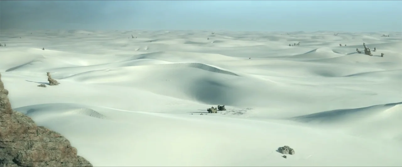 Monster Hunter (2020) movie still: establishing — An immense expanse of bright white sand dunes stretches to the hazy horizon line. Two small…