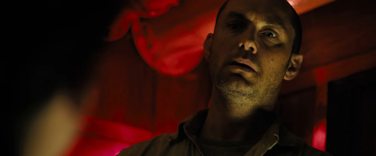 Black Sea (2014) movie still: closeup — The interior space is cast in shadows with vibrant red light reflecting off surfaces. A man with a short…