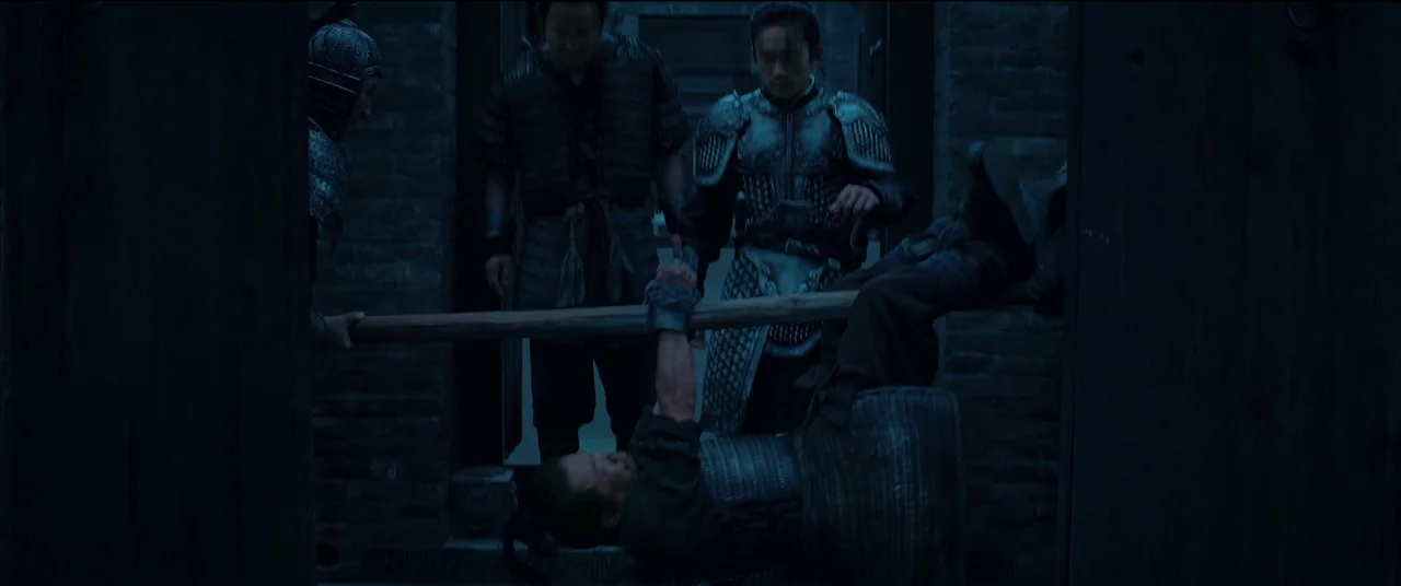 Full River Red (2023) movie still: medium — A dark stone passageway with brick walls and low lighting levels. Three armored men transport a person…