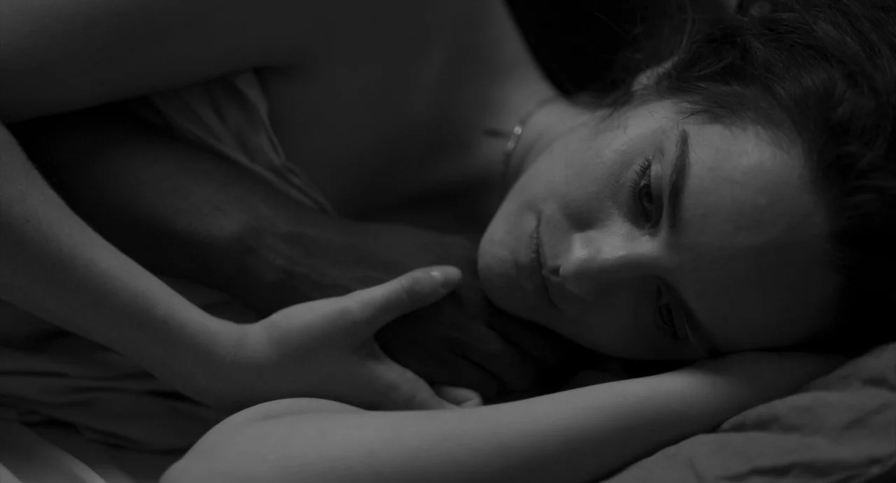 Paris, 13th District (2021) movie still: closeup — A dark bedroom setting features a person resting under soft white bed linens. The subject lies on…