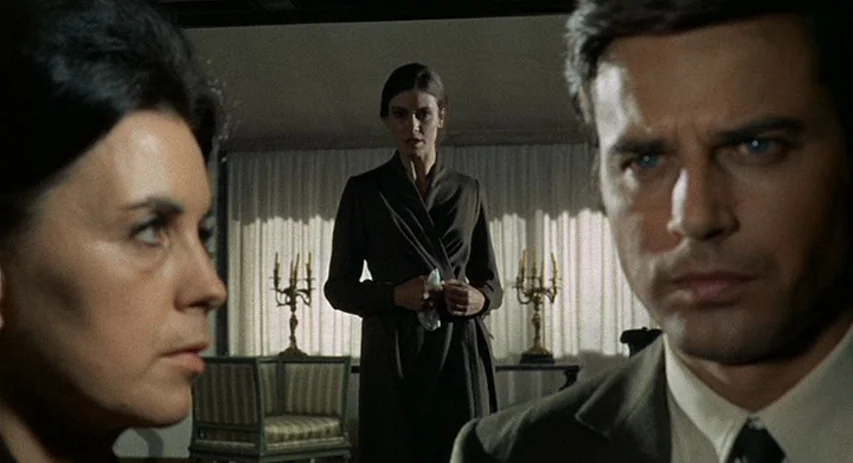 Perversion Story (1969) movie still: medium — A well-furnished room features draped curtains over a large window with two decorative candelabras.…