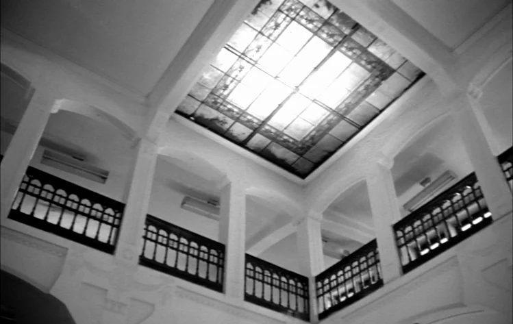 Werckmeister Harmonies (2000) movie still: establishing — A multi-level building interior features white arched columns and dark iron balcony…