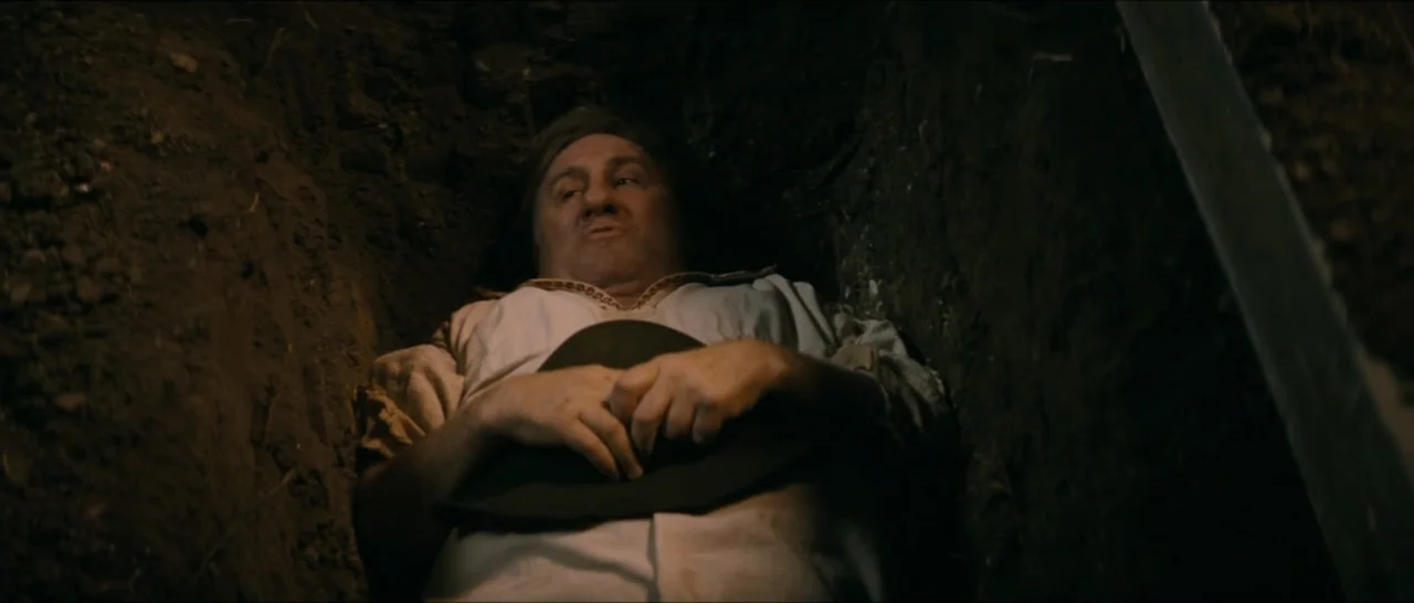 A Farewell to Fools (2013) movie still: medium — A man lies inside a narrow, deep trench carved into dark, compacted earth. The subject wears a…