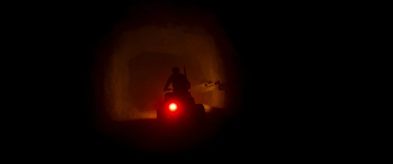 Mandy (2018) movie still: wide — A dark, rough-hewn tunnel with stone walls stretches deep into the black distance. A person on a small vehicle…