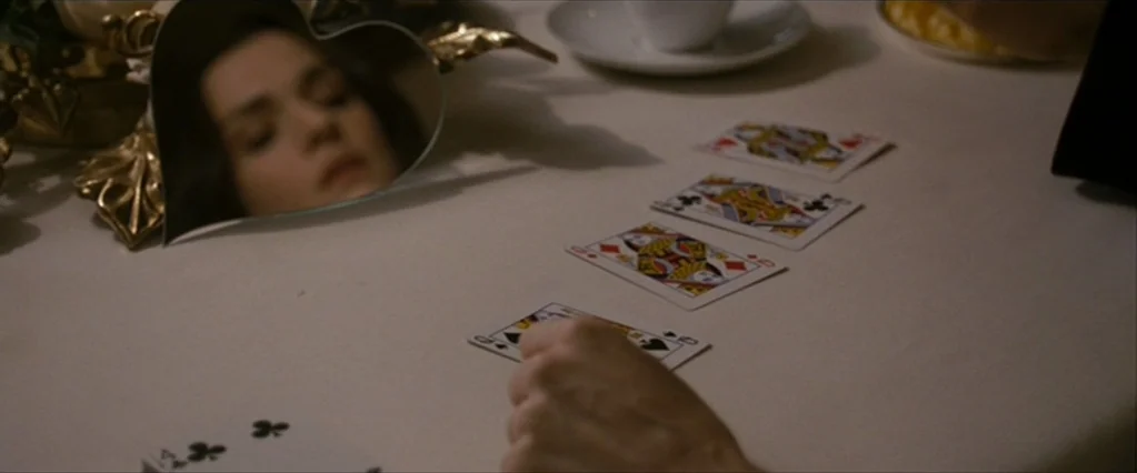 The Brothers Bloom (2008) movie still: medium — A set table with a white cloth holds playing cards and a tea setting. A hand arranges cards on the…