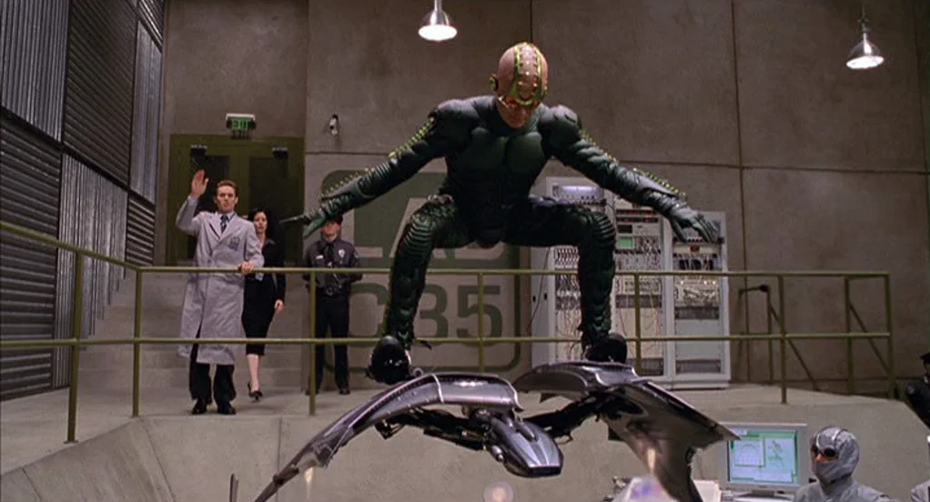 Spider-Man (2002) movie still: fullbody — A sterile industrial research room with concrete walls and visible control panels behind stairs. A man in…