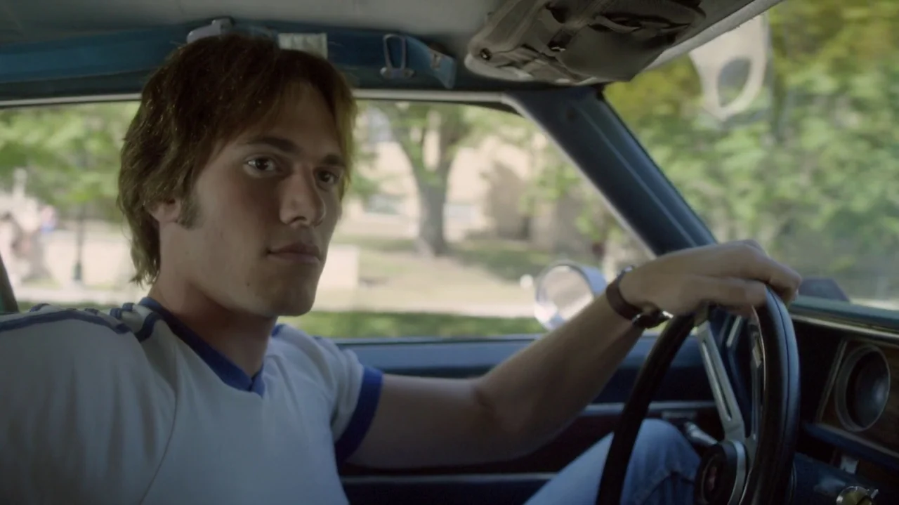 Everybody Wants Some!! (2016) movie still: medium — The interior of a vintage car shows a young man driving during the day. He holds the steering…