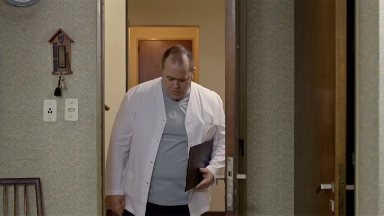 Heaven Sent (1994) movie still: medium — A residential hallway features floral patterned wallpaper and wooden door frames. A man in a medical coat…