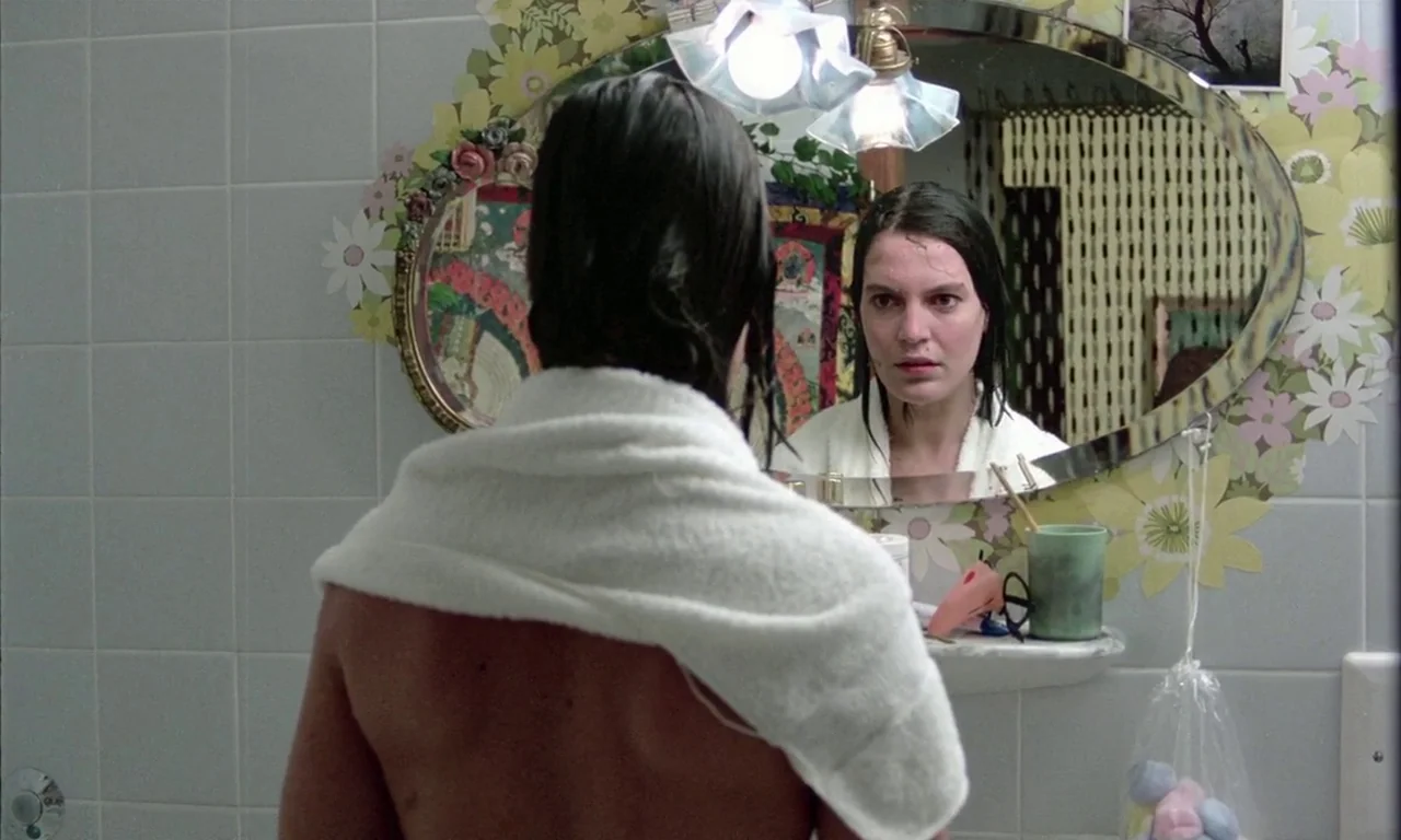 The Lost Honour of Katharina Blum (1975) movie still: medium — A bathroom with pale blue square tiles and floral wallpaper surrounding the vanity…