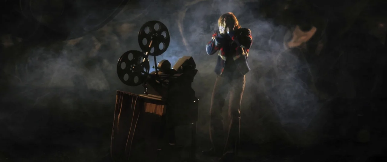 The Editor (2014) movie still: medium — A dark, smoke-filled room is dominated by a standing vintage film projector. A man stands beside the…