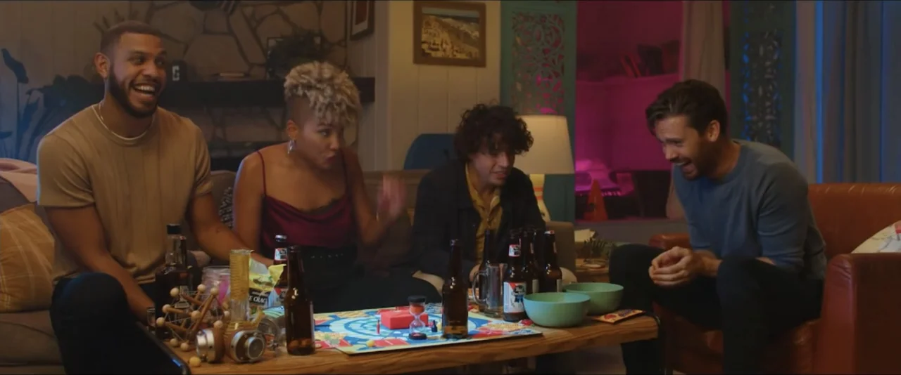 Gatlopp: Hell of a Game (2022) movie still: medium — A cozy living room contains a wooden coffee table cluttered with drinks and games. Four friends…