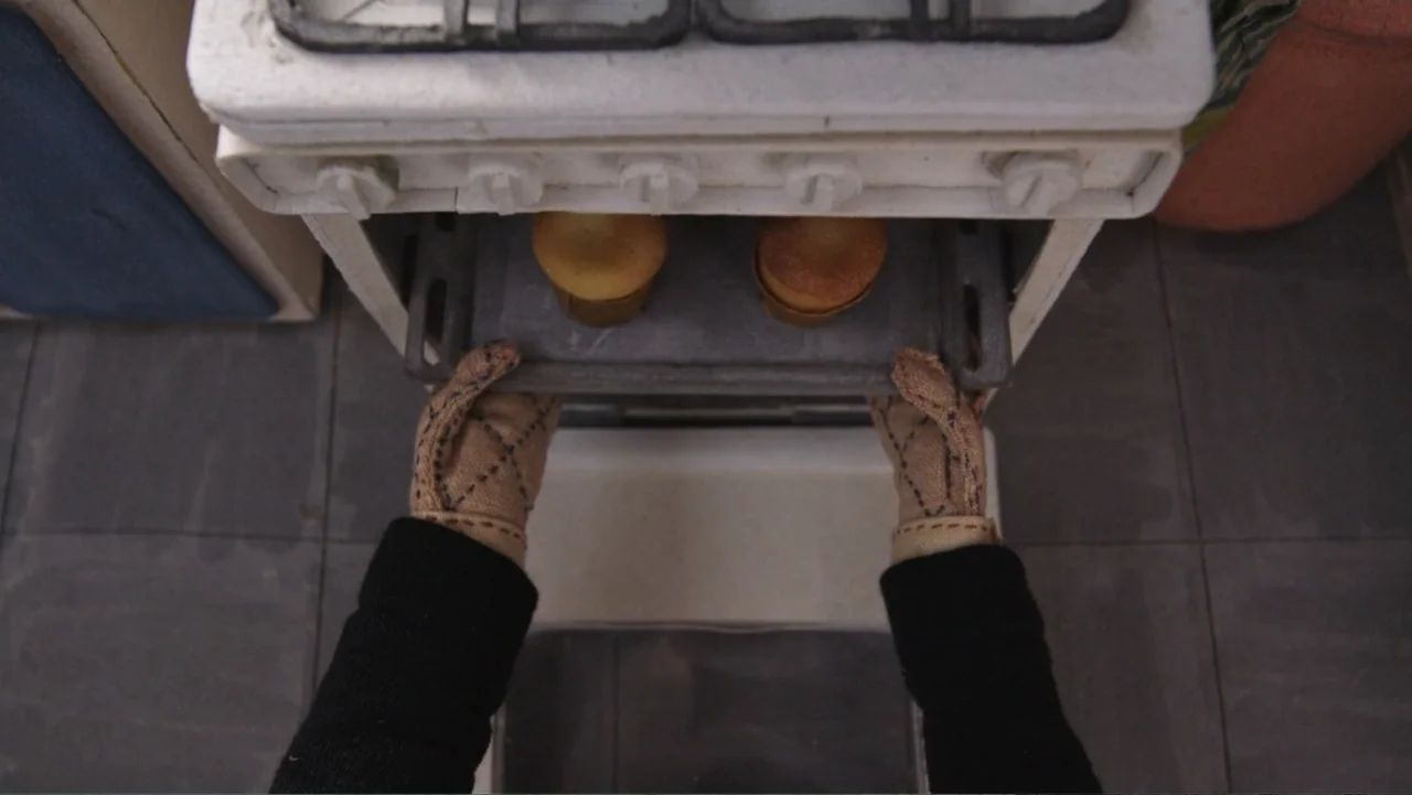 Bestia (2017) movie still: medium — An overhead view inside a kitchen shows a person using oven mitts to retrieve food. Two small baked goods sit on…