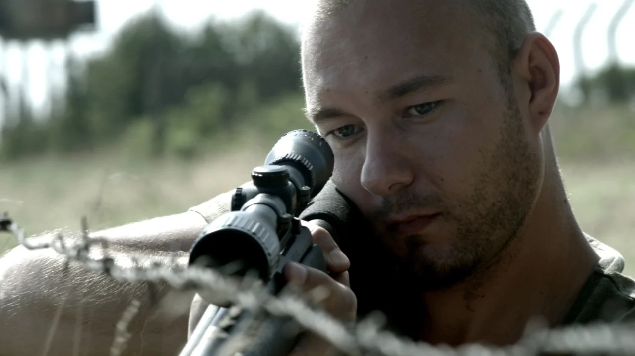 6 Bullets (2012) movie still: closeup — An outdoor field with blurred green vegetation in the background. A man with a buzzed haircut looks intently…