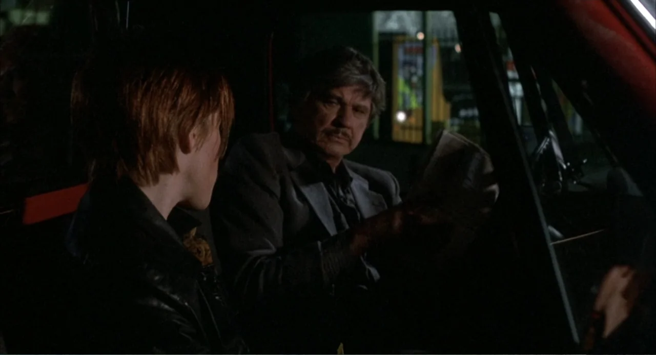 Murphy's Law (2009) movie still: medium — A dark car interior at night with a man and a woman present. The man examines a paper document while the…