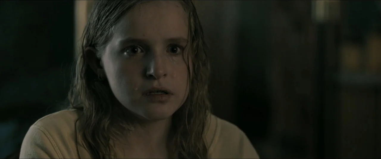 It Feeds (2025) movie still: closeup — A dimly lit indoor space with low-key illumination on a subject. A young girl stares ahead with tears visible…