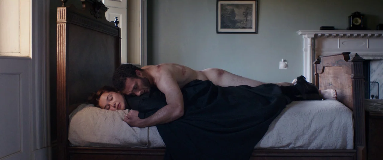 Lady Macbeth (2016) movie still: medium — A nineteenth-century room features a wooden bed frame, a mantelpiece, and a framed picture. A man and a…