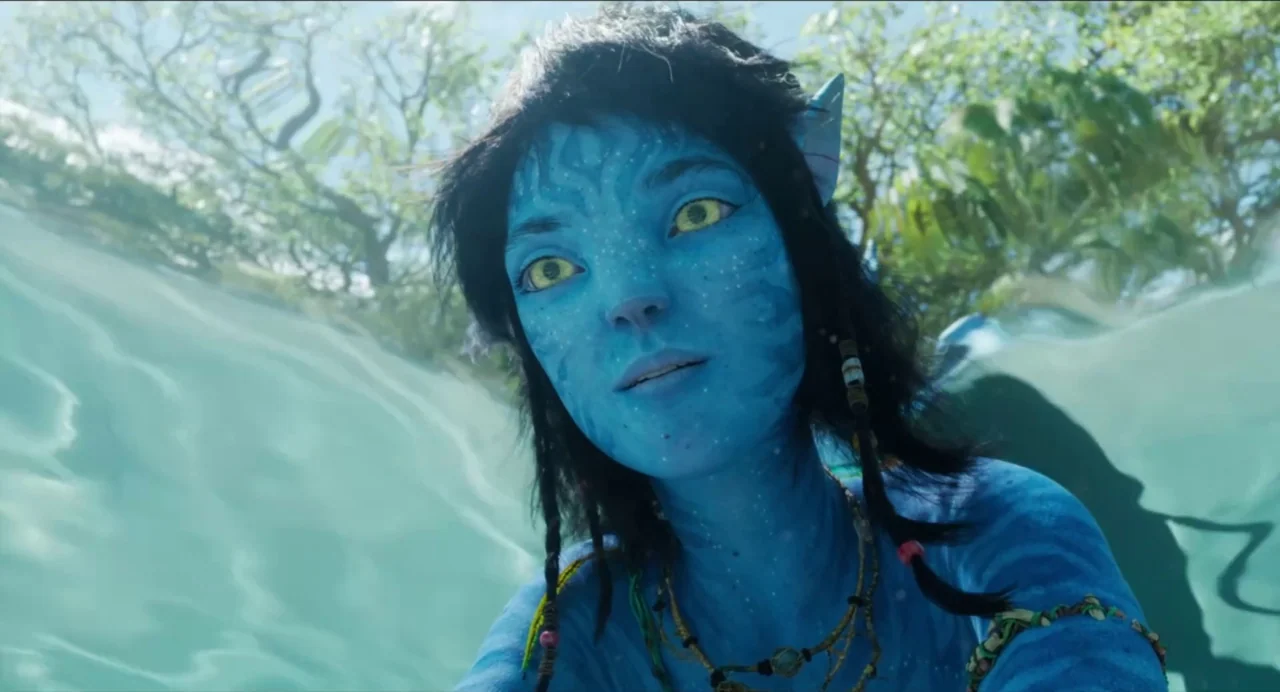 Avatar: The Way of Water (2022) movie still: closeup — A blue-skinned Na'vi female emerges from crystal clear tropical water. Sunlight filters…