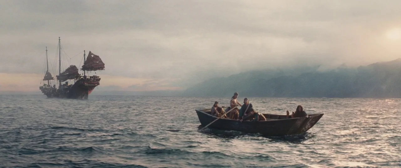 Silence (2016) movie still: wide — An open expanse of sea with a large junks-style sailing vessel in the distance. Five men sit in a small wooden…
