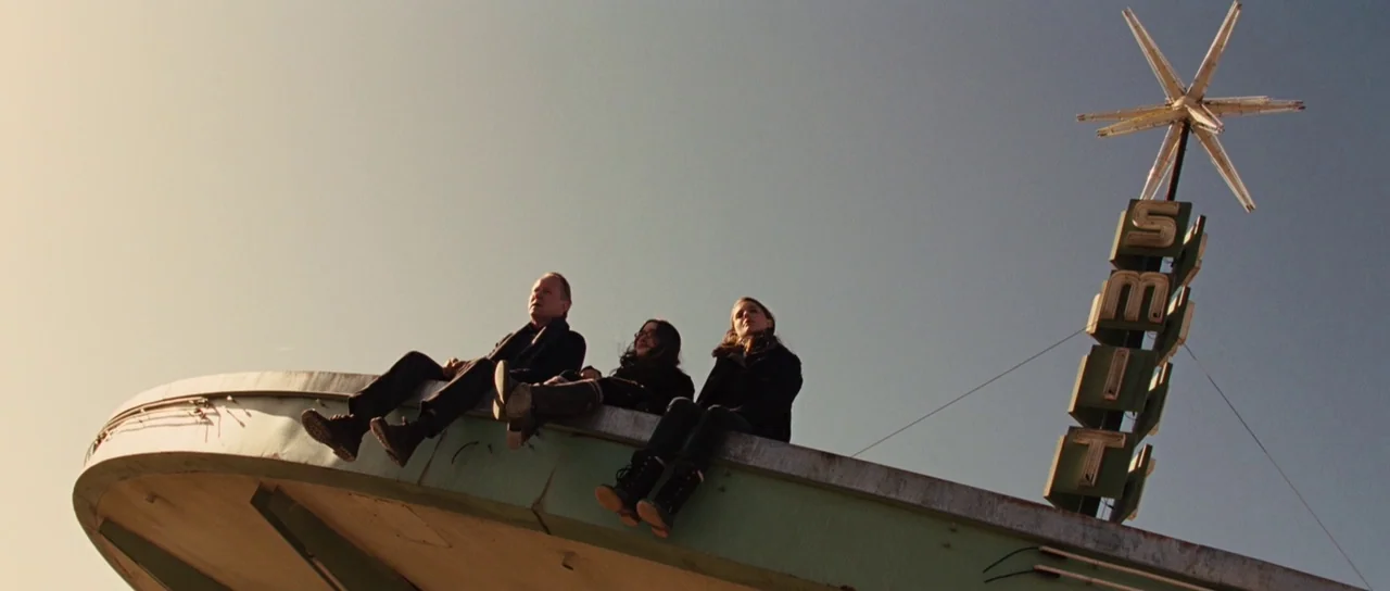 Thor (2011) movie still: wide — Three people sit on the edge of a circular concrete structure with a vertical sign. A large metallic star ornament…