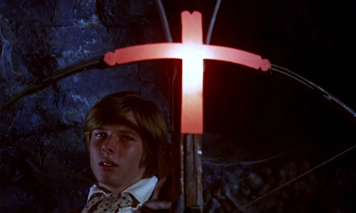 Vampire Circus (1972) movie still: medium — A dark, rocky underground chamber features human bones scattered in the background shadows. A young man…