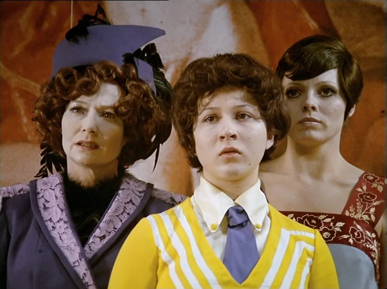 The Bitter Tears Of Petra Von Kant (1972) movie still: medium — Three women in distinct 1970s attire stand before a warm-toned painted backdrop. The…