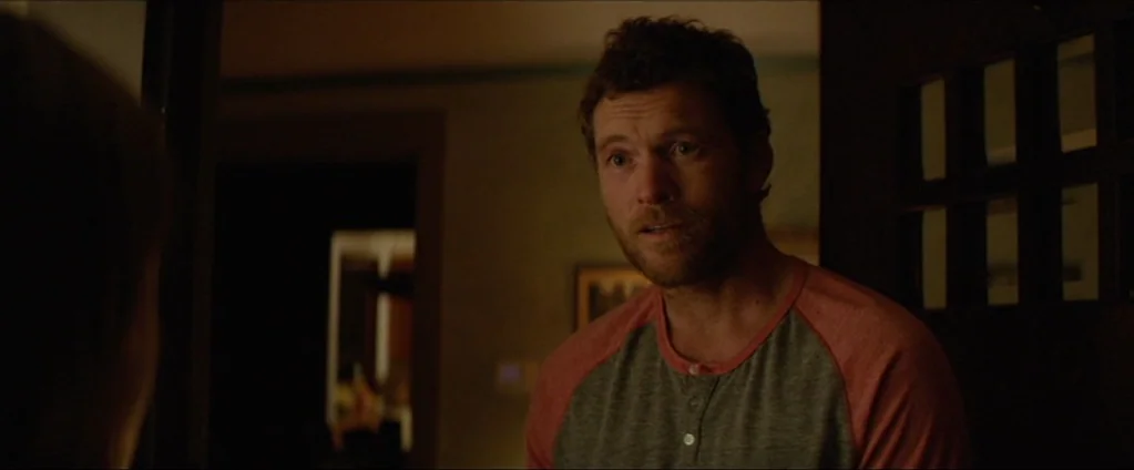 Cake (2014) movie still: medium — A man stands in a dark indoor doorway transition between two rooms. He looks toward an unseen person in the…