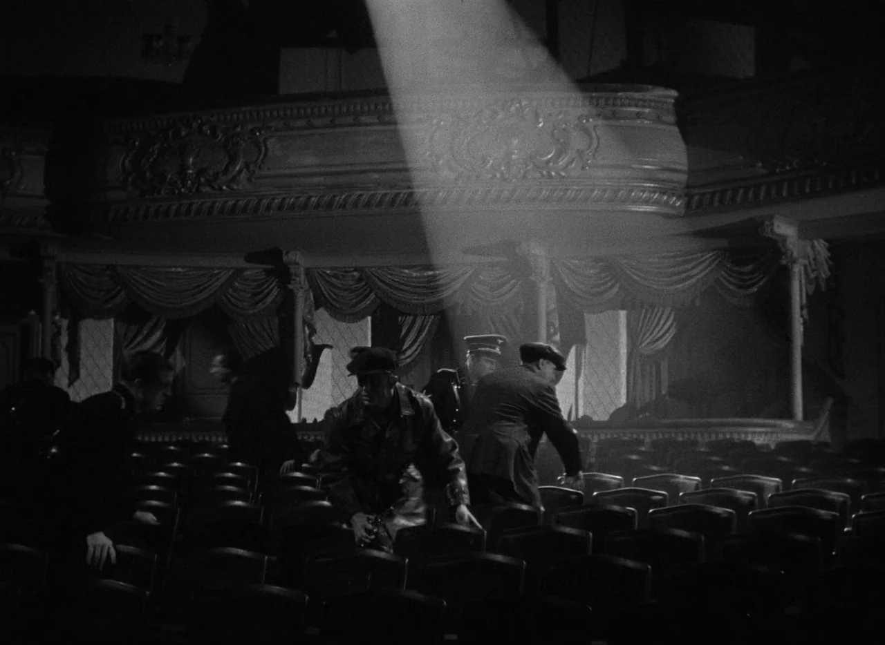 To Be or Not To Be (1942) movie still: wide — An ornate theater with curved balconies and draped curtains sits in near total darkness. Several men…