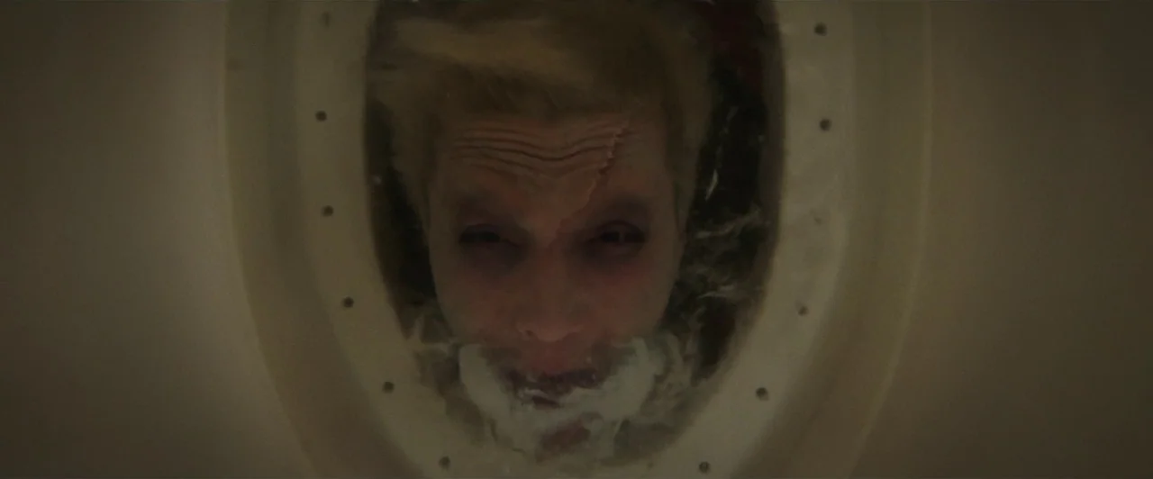 Aquaman (2018) movie still: closeup — A close overhead shot looking directly down into a white, circular plastic basin. A blonde man is submerged in…