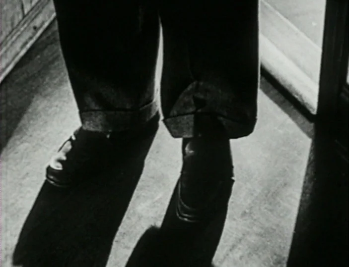 Meshes of the Afternoon (1943) movie still: closeup — A dark wooden floor is illuminated by a diagonal beam of hard light. A pair of cuffed trousers…