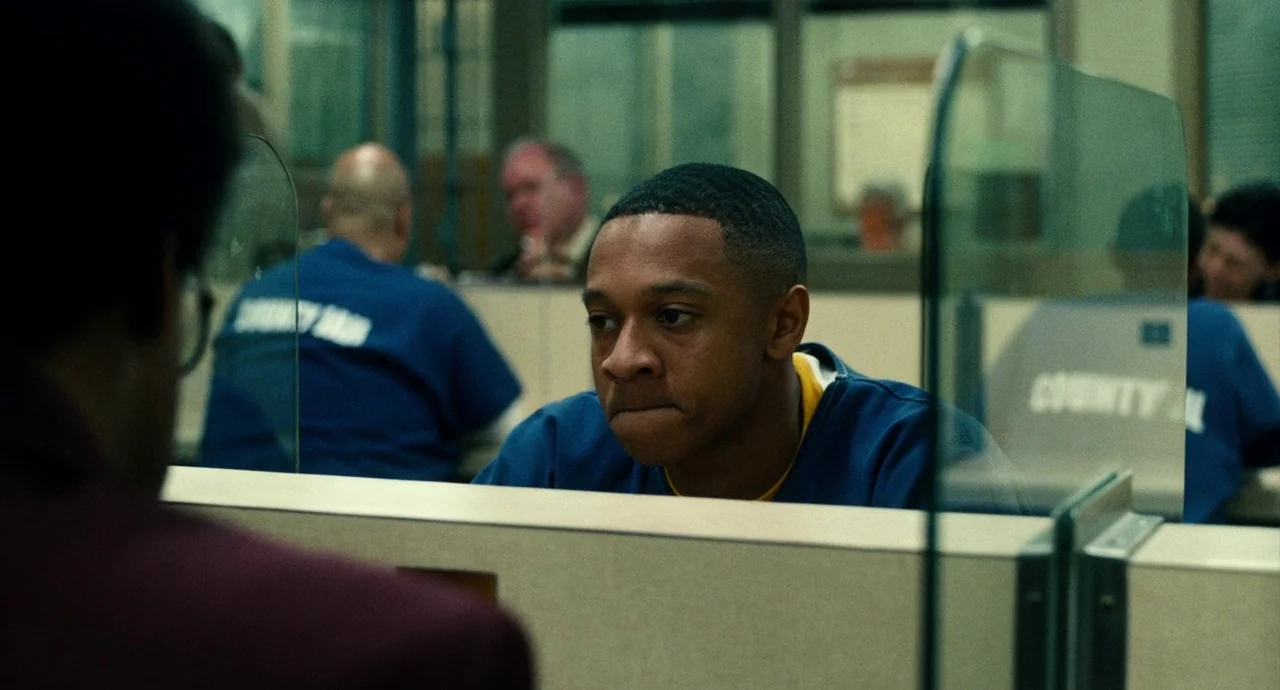 Roman J. Israel, Esq. (2017) movie still: medium — A jail visiting room with rows of partitioned seating areas separated by glass panels. A young…