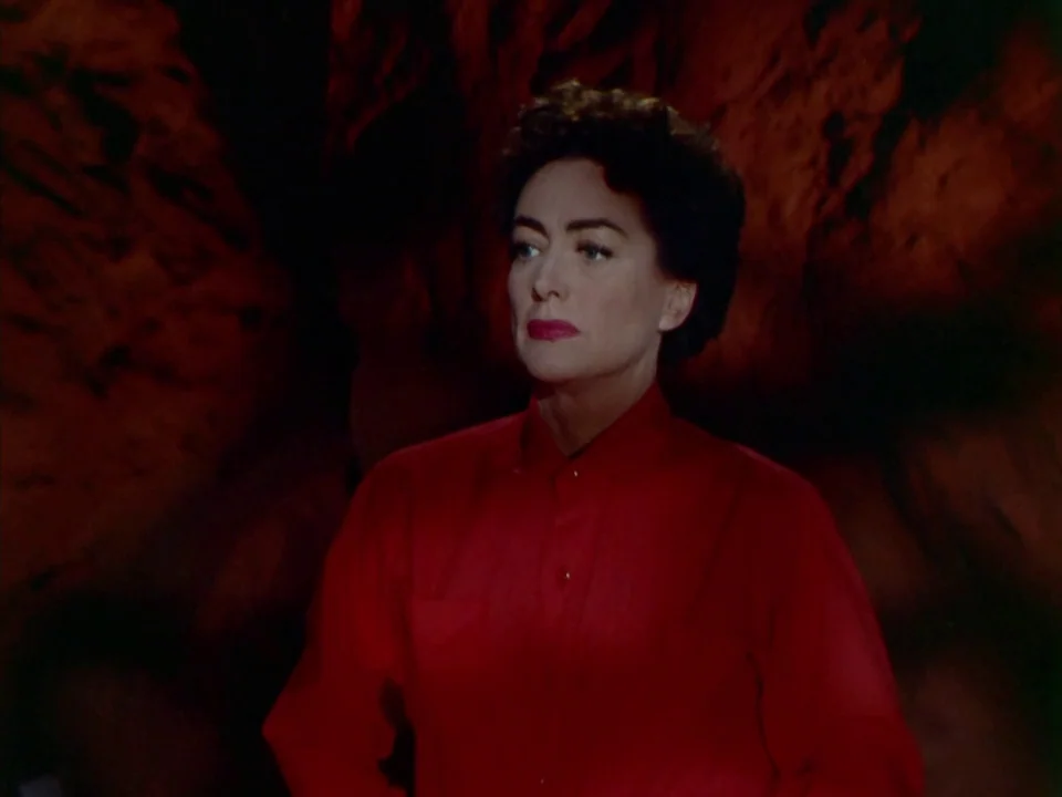 Johnny Guitar (1954) movie still: medium — A woman in a red shirt stands against a dark, rocky, cavernous wall. She gazes off-screen to the left…