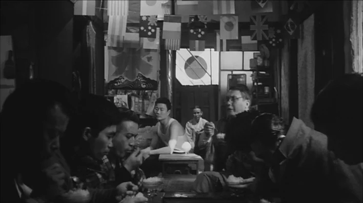 Death By Hanging (1968) movie still: medium — A crowded small shop interior features rows of national flags hanging from the ceiling. Multiple men…